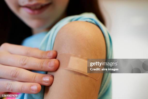 girl points to band-aid on her arm after doctor gives her a vaccine - vaccine bandage stock pictures, royalty-free photos & images