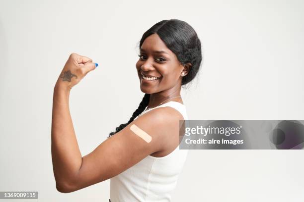 short haired black woman wearing a white shirt smiling and flexing his arm, with a white background. wellness concept - black woman happy white background foto e immagini stock