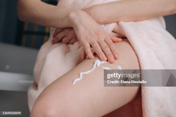 woman applies moisturizing lotion to her thigh skin, body cream after showering - cellulite stock pictures, royalty-free photos & images