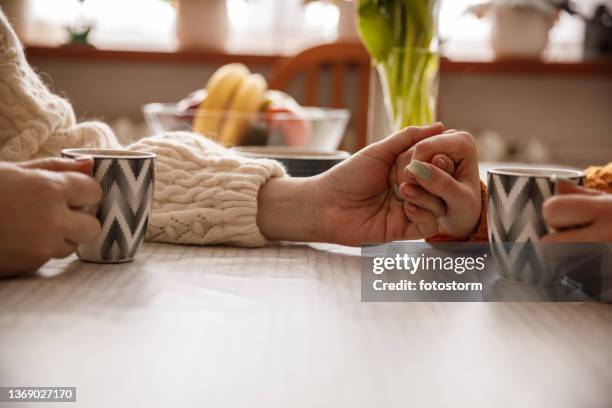 mature woman holding hands with her daughter while having coffee together - representing stock pictures, royalty-free photos & images