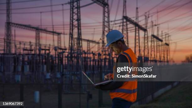 confident male engineer using a laptop in front of electric power station - elétrico imagens e fotografias de stock