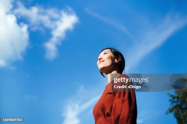 low angle portrait of beautiful smiling young asian woman standing against beautiful clear blue sky, looking up to sky enjoying nature and sunlight. freedom in nature. connection with nature - hope concept bildbanksfoton och bilder