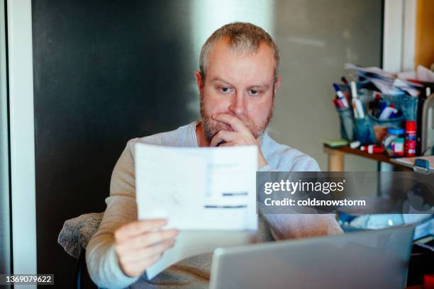 hombre preocupado revisando las facturas en casa - facturación fotografías e imágenes de stock