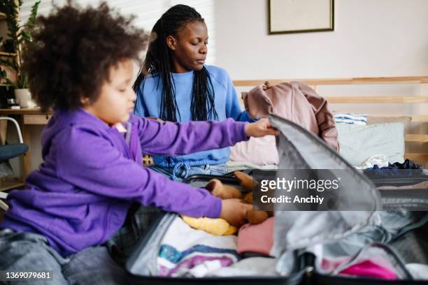 young multiethnic family packing suitcases for vacation - mother and daughter making the bed stock pictures, royalty-free photos & images