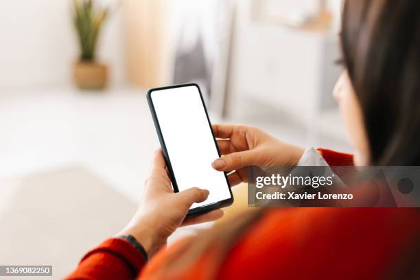 unrecognizable young woman holding a mobile phone with white screen at home - holding iphone stock pictures, royalty-free photos & images