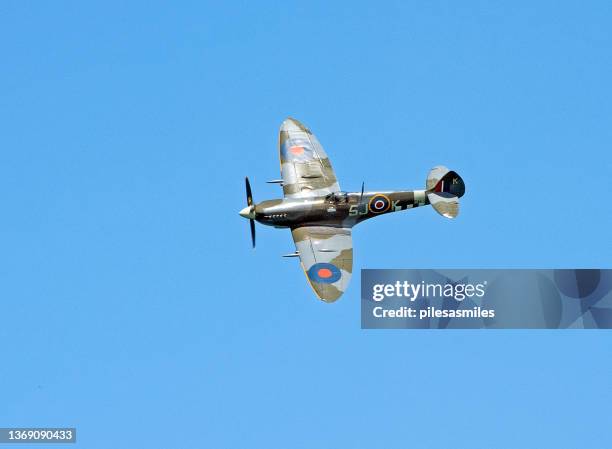 spitfire in ww2 camouflage banking to port in clear blue sky - spitfire stockfoto's en -beelden