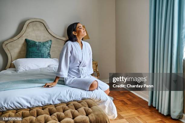 Shot of an attractive young woman sitting on the bed in her hotel room and looking contemplative in the morning
