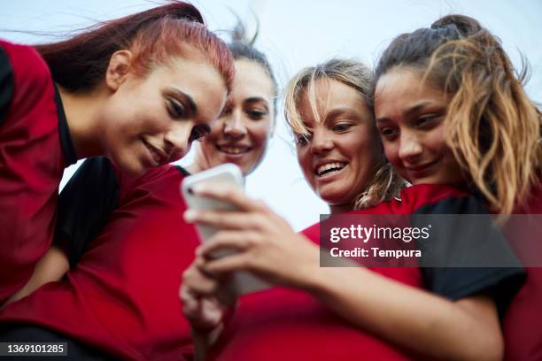 a female soccer team share a phone to check on social media. - football phone stock pictures, royalty-free photos & images