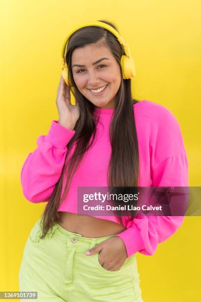 midsection of a 18 year old woman with colorful casual clothes and red glasses listening music with wireless headphones - fondo amarillo stock pictures, royalty-free photos & images