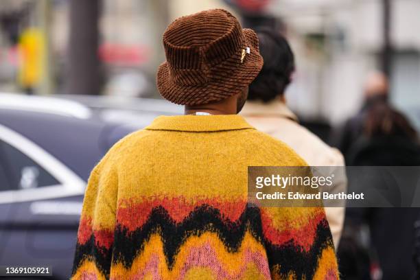Guest wears a dark brown ribbed velvet bob with a gold brooch, a yellow with red / black / yellow / pink wavy print pattern pullover, black pants,...