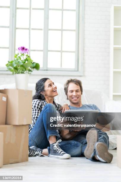 shot of beautiful happy couple looking decoration ideas on a laptop, while  sitting next to the moving boxes on the floor in their new home. - new boyfriend stock pictures, royalty-free photos & images