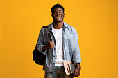 Positive millennial black man student with books on yellow