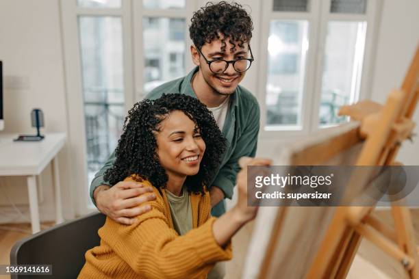 young couple enjoying spending time together painting and using technology - house for an art lover stock pictures, royalty-free photos & images