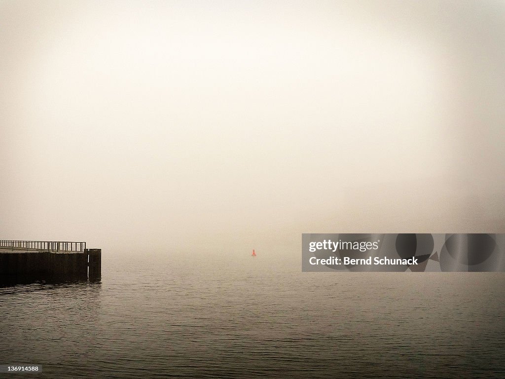 Pier and red buoy in fog