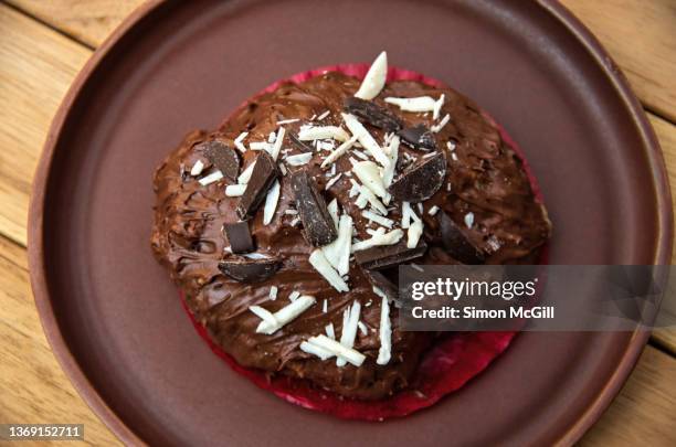 chocolate iced scone decorated with dark and white chocolate pieces on a plate on an outdoor cafe table - chocolate chip cookie stock-fotos und bilder