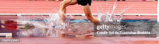 close-up of male legs running a steeplechase race and splashing water as he passes through the pit on the athletic field - carreras de obstáculos prueba en pista fotografías e imágenes de stock