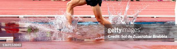 close-up of male legs running a steeplechase race and splashing water as he passes through the pit on the athletic field - steeplechase track event 個照片及圖片檔