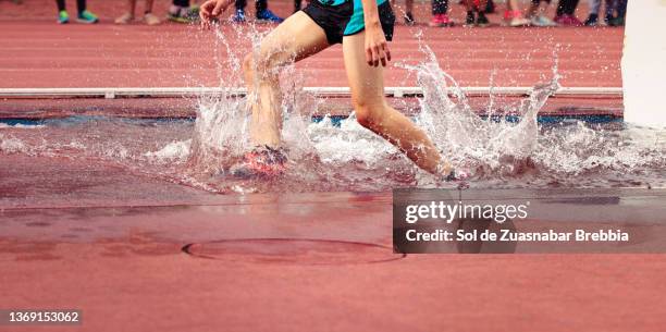 close-up of male legs running a steeplechase race and splashing water as he passes through the pit on the athletic field - hindernislauf laufdisziplin stock-fotos und bilder