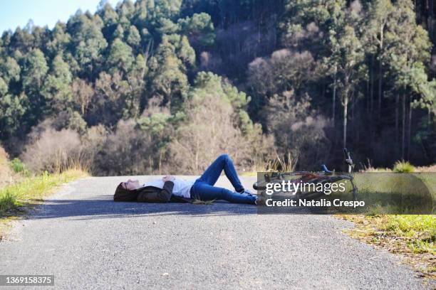 young man lying on a road next to bicycle. - radfahren männer stock-fotos und bilder