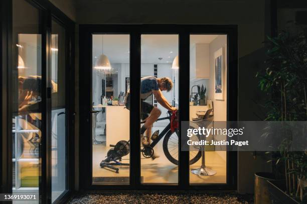 man using his indoor bike turbo trainer at home in the evening - photographed through window stockfoto's en -beelden