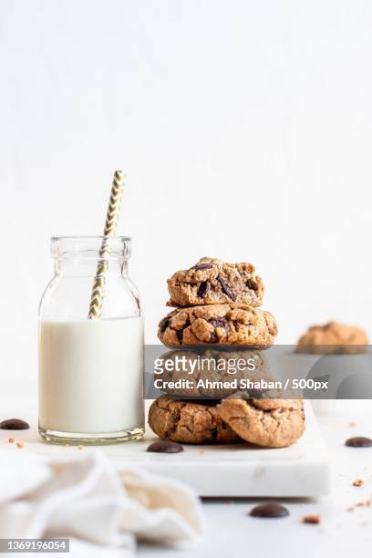 close-up of cookies with milk on table against white background - chocolate chip cookie stock-fotos und bilder