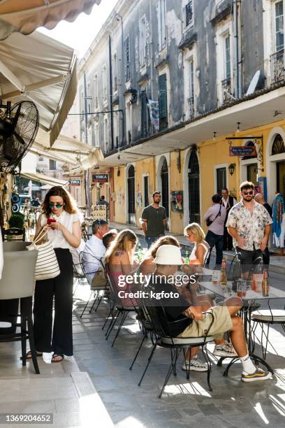 tourists sitting at tables of greek taverna in a sunny day between old houses of corfu town, corfu greece - corfu town stock pictures, royalty-free photos & images