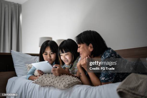 mutter und kinder schauen sich einen film auf dem digitalen tablet auf dem bett zu hause an - asian watching movie stock-fotos und bilder