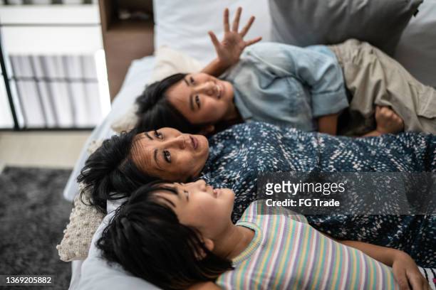 mother talking stories to her kids in bed at home - storyteller 個照片及圖片檔
