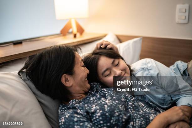 mother laying down with daughter in bed at home - teen sleeping bedroom stock pictures, royalty-free photos & images