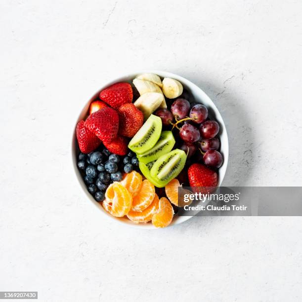 bowl of fresh fruit (grapes, bananas, strawberries, grapes, oranges, and kiwi) on white background - obstschale stock-fotos und bilder