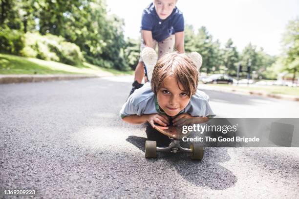 boy pushing brother on skateboard down the street - 11 11 road stock-fotos und bilder