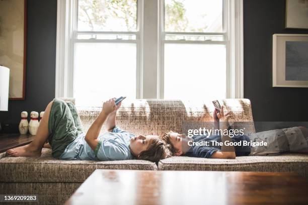 brothers relaxing on sofa in living room at home - child smartphone stock pictures, royalty-free photos & images