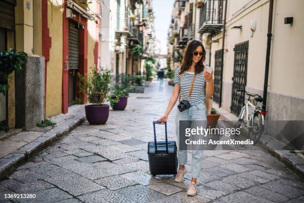young woman pulls suitcase down cobblestone street - holiday suitcase stockfoto's en -beelden