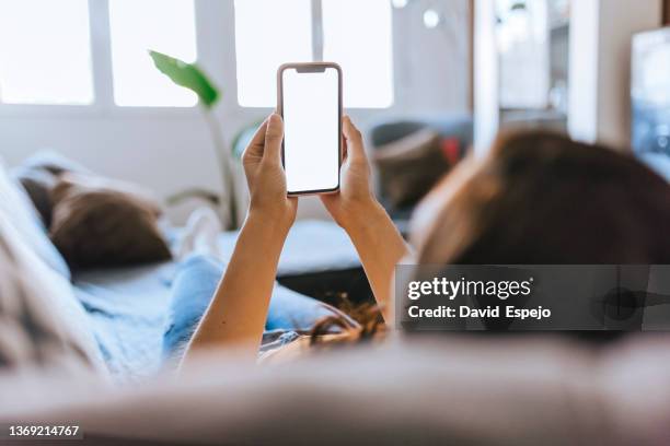 unrecognizable woman sitting on the sofa at home watching the mobile phone. - frau mit handy screen stock-fotos und bilder