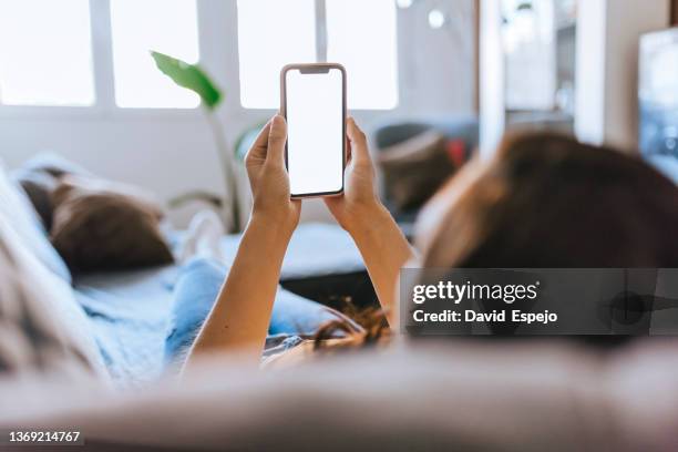 unrecognizable woman sitting on the sofa at home watching the mobile phone. - regarder par dessus son épaule photos et images de collection