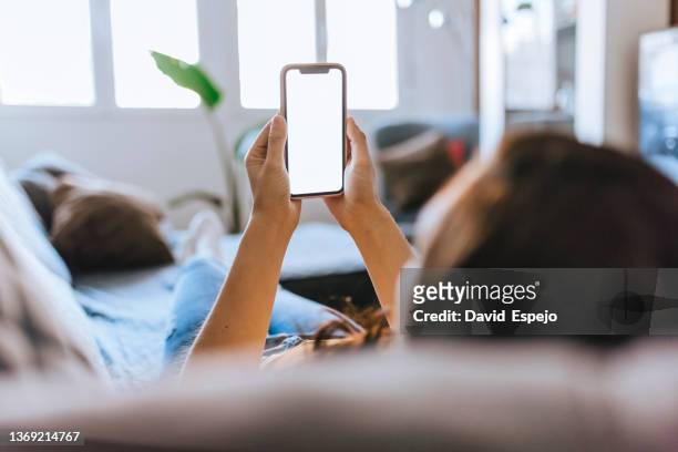 unrecognizable woman sitting on the sofa at home watching the mobile phone. - woman looking over shoulder stock pictures, royalty-free photos & images