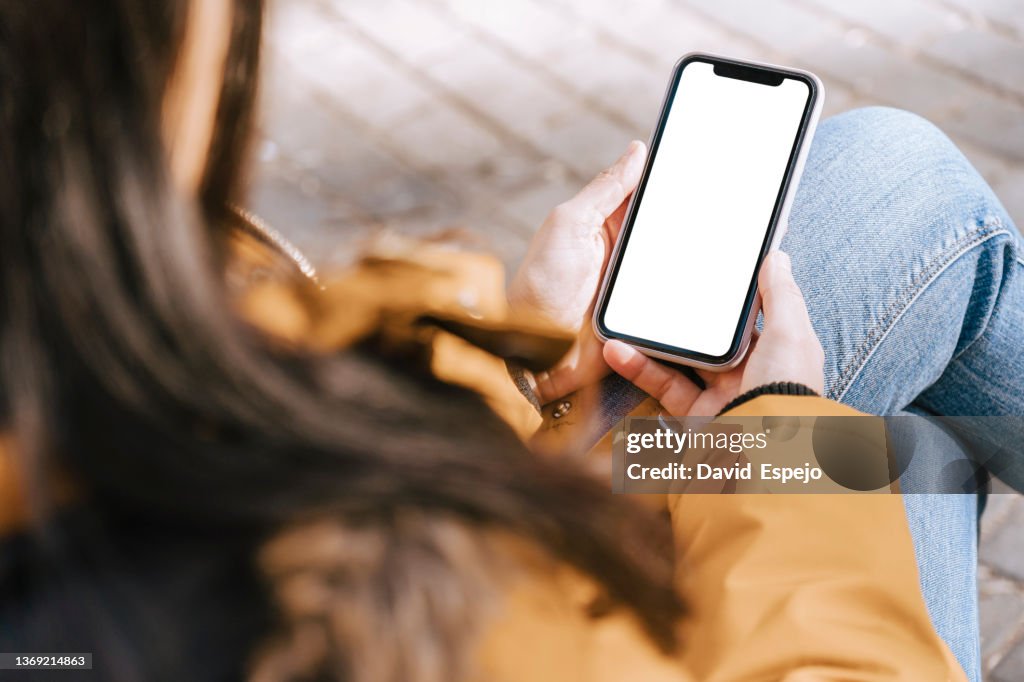 Unrecognizable woman sitting on a street bench while ordering food for delivery.
