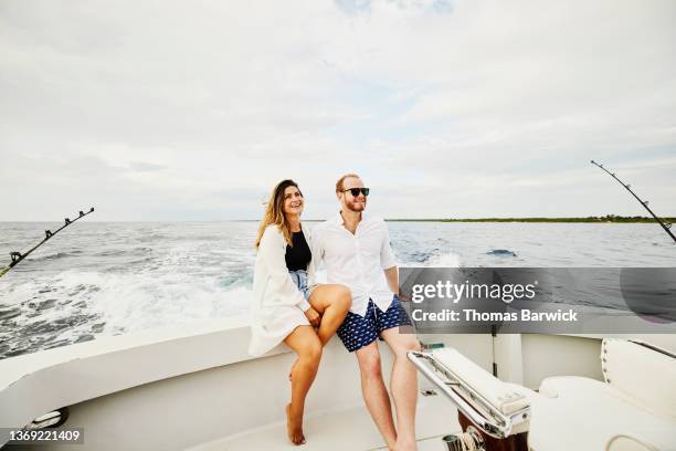 wide shot of smiling couple sitting on stern of sport fishing boat - small boat stock pictures, royalty-free photos & images