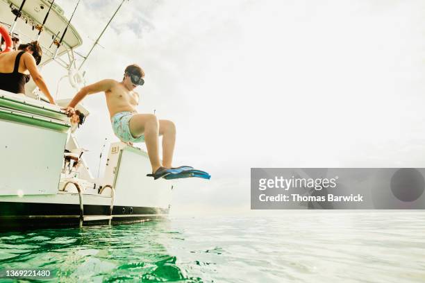 Wide shot of teenage boy jumping into tropical sea from boat to go snorkeling