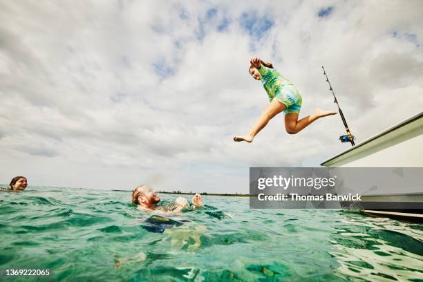 wide shot view from water of daughter jumping to father from side of boat in tropical sea - jumping of boat photos et images de collection