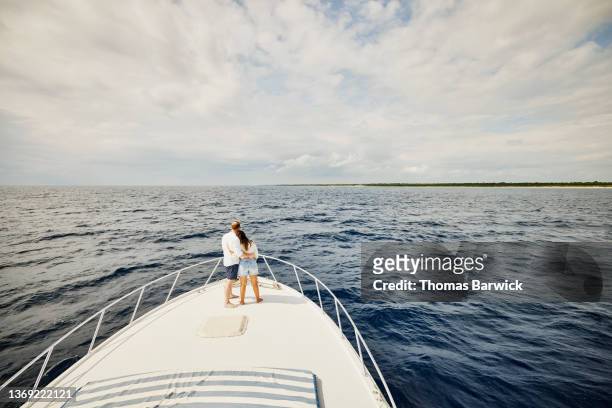 wide shot of couple embracing on bow of yacht while on vacation - yachting lifestyle stock pictures, royalty-free photos & images