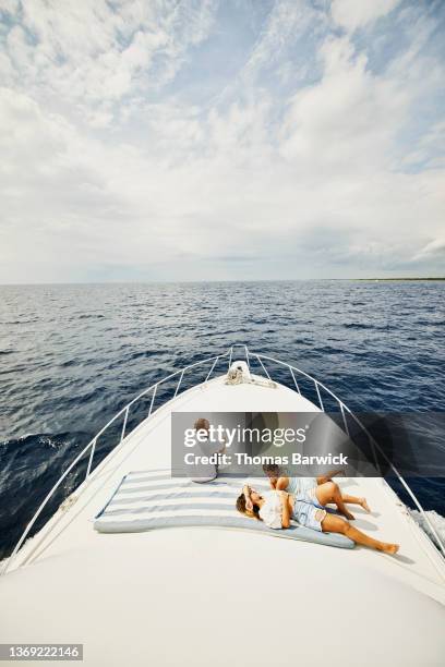 wide shot of family relaxing on bow of yacht while on vacation - schiffsbug stock-fotos und bilder