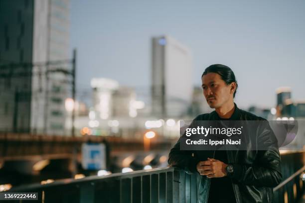 man contemplating in city at night, tokyo - レザージャケット ストックフォトと画像