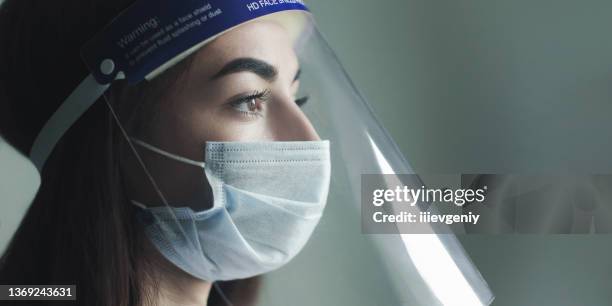 a young doctor portrait in protective mask on gray background. medical specialist in professional uniform. face shield. beautiful brunette girl in protective gear. confident nurse. panoramic crop - face mask protective workwear imagens e fotografias de stock