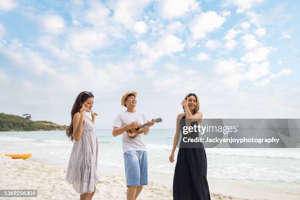 friends enjoying music and playing guitar while relaxing on the beach - lens flare young people dancing on beach stock pictures, royalty-free photos & images