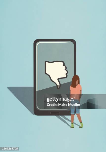 sad girl standing next to thumbs down icon on smart phone screen - cyberbullying stock-grafiken, -clipart, -cartoons und -symbole