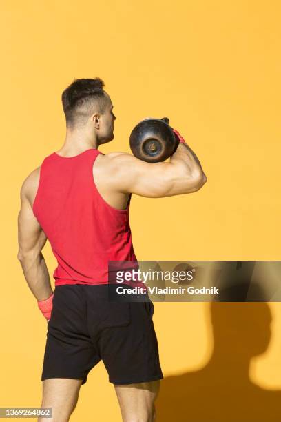 strong, athletic man with kettle bell against yellow background - bíceps fotografías e imágenes de stock