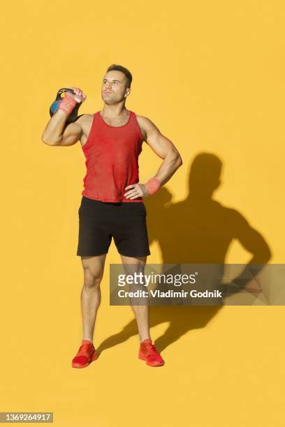 studio portrait athletic man in red sportswear with kettle bell against yellow background - bodybuilder posing stock pictures, royalty-free photos & images