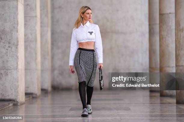 Natalia Verza wears a white with black embroidered logo cropped shirt from Prada, a gold bracelet, a high waist black with embroidered rhinestones...