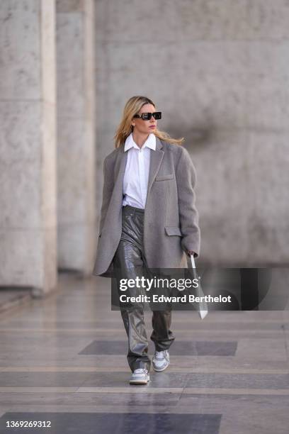 Natalia Verza wears black sunglasses, a silver and black pendant earring from Prada, a white shirt from Karl Lagerfeld, a gray oversized felt /...